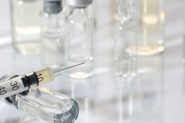 Glass vial and syringe with medication on white table, closeup. Space for text
