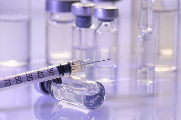Glass vial and syringe with medication on white table, closeup. Space for text