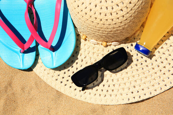 Straw hat, sunglasses, flip flops and refreshing drink on sand, above view. Beach accessories