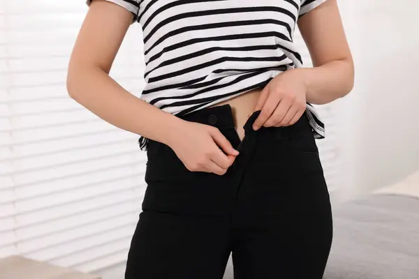Woman trying to fit into her black jeans at home, closeup