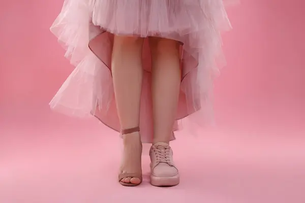 Woman wearing high heeled shoe and sneaker on pink background, closeup. Glamour vs comfort concept