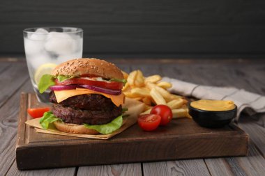 Köfteli lezzetli çizburger, patates kızartması, sos ve domatesler ahşap masada.