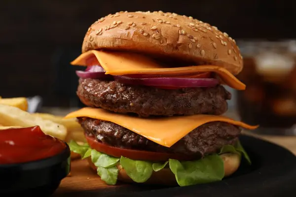 Delicious burger with meat cutlets, cheese, vegetables and lettuce against blurred background, closeup