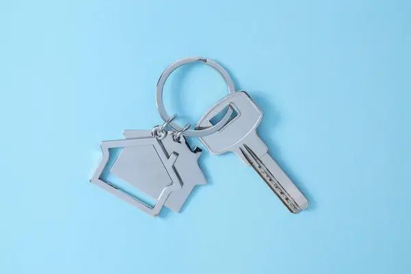 Key with keychain in shape of house on light blue background, top view