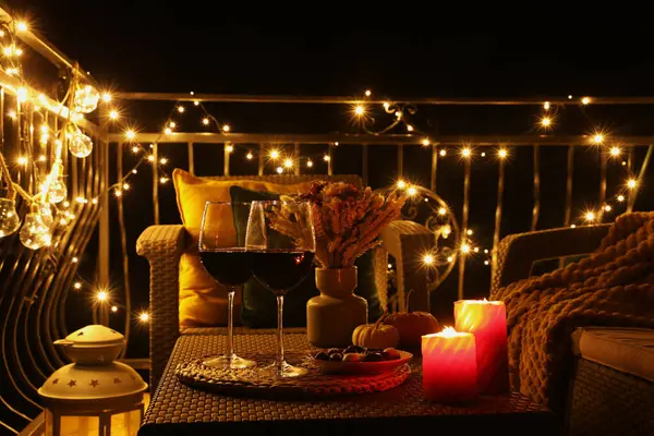 Glasses of wine, burning candles and decor on rattan table. Autumn evening on terrace
