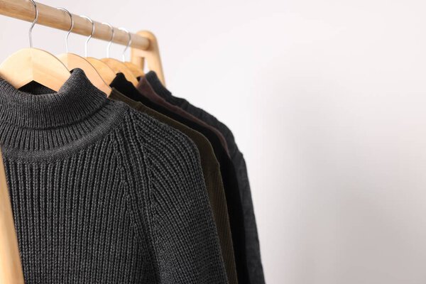 Rack with different casual sweaters on light background. Space for text
