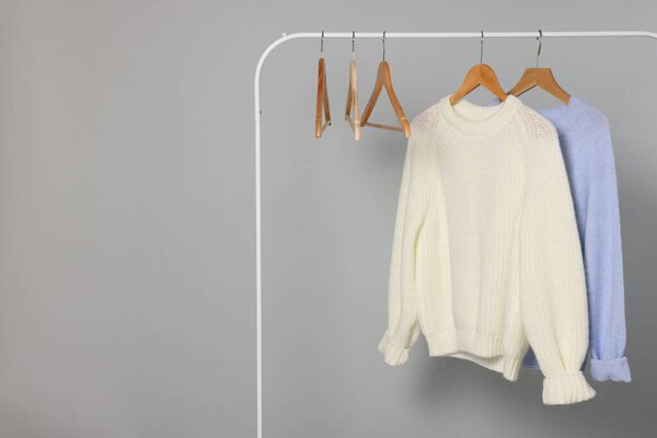 Rack with warm sweaters and hangers on light grey background. Space for text