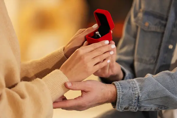 Man with engagement ring making proposal to his girlfriend against blurred background, closeup