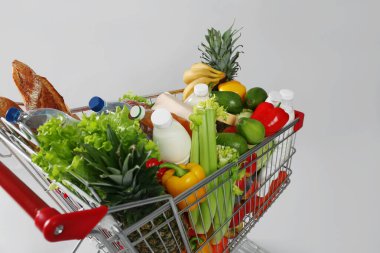Gri arka planda alışveriş arabası dolusu yiyecek.