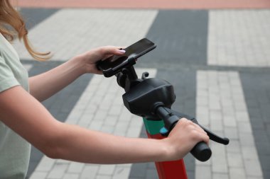 Modern elektrikli scooter kullanan bir kadın açık havada akıllı telefon kullanıyor.