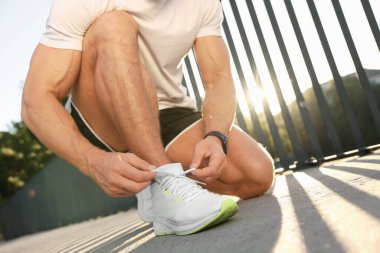 Güneşli bir günde dışarı çıkmadan önce ayakkabı bağcıklarını bağlayan adam, yakın çekim.