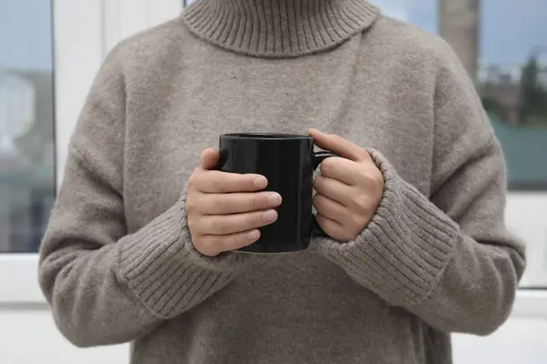 Woman holding black mug indoors, closeup view