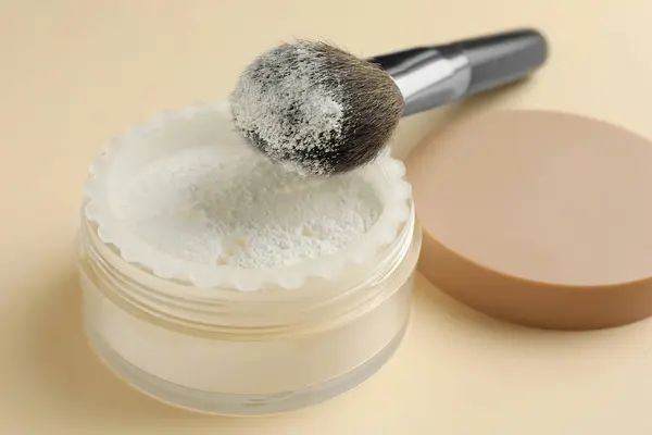 Rice loose face powder and makeup brush on beige background, closeup