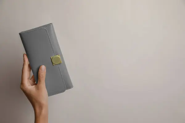 Woman holding grey leather purse on light background, closeup. Space for text
