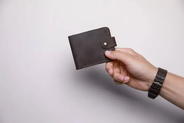 Man holding leather wallet on light background, closeup. Space for text