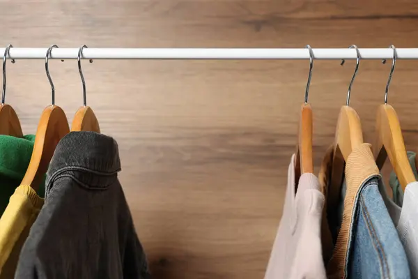 Hangers with stylish women`s clothes on rack near wooden wall, closeup