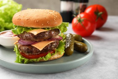 Açık gri masada servis edilen köfteli, peynirli ve sebzeli lezzetli hamburger.