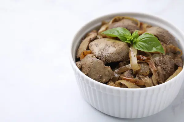 Delicious fried chicken liver with onion and basil in bowl on white table, closeup. Space for text