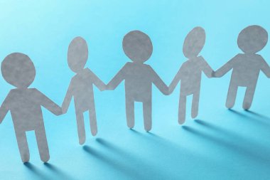 Takım çalışması konsepti. Açık mavi arka planda el ele tutuşan insanların kağıt figürleri