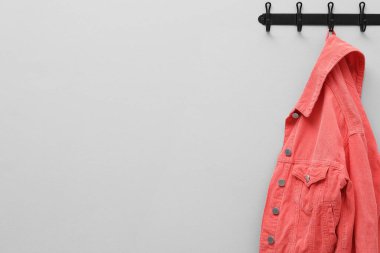 Açık gri duvarda askıda asılı mercan ceketi, metin için boşluk