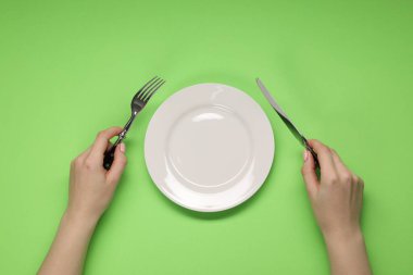 Yeşil masadaki boş tabağın yanında çatal ve bıçak tutan kadın.