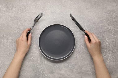 Çatal ve bıçak taşıyan kadın gri desenli masada, boş tabağın yanında.