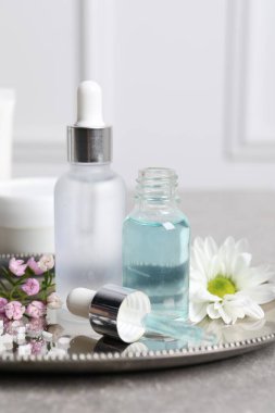Kozmetik serumu şişeleri ve gri masada güzel çiçekler.