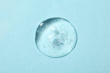 Açık mavi arkaplanda kozmetik serumu damlası, üst görünüm