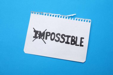 Motivasyon konsepti. Açık mavi arkaplanda I ve M harflerinin üzerinden geçerek İmkânsızdan Olanaksız kelimesine çevirilmiş kağıt, üst görünüm