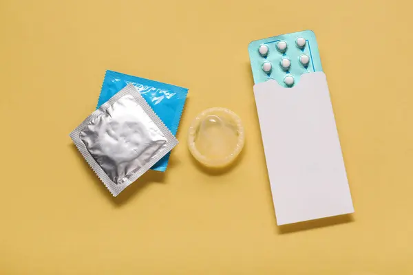 Condoms and birth control pills on yellow background, flat lay. Choosing method of contraception