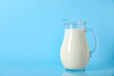 Açık mavi arkaplanda bir sürahi taze süt, metin için boşluk