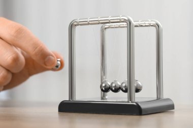 Newton 'un beşiğiyle oynayan adam arka planda ışığa karşı oynuyor, yakın plan. Enerji korunumunun fizik yasası