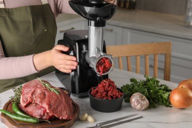 Mutfaktaki beyaz mermer masada elektrikli et öğütücüsüyle kıyma yapan kadın, yakın plan.