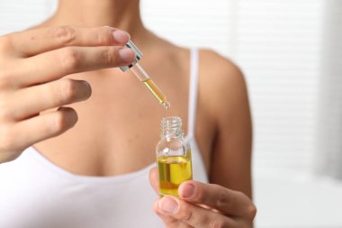 Hafif arka planda kozmetik serumu şişesi olan kadın, yakın plan.