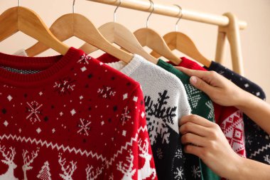 Bej duvarın yanındaki raftan Noel süveterini seçen kadın, yakın plan.