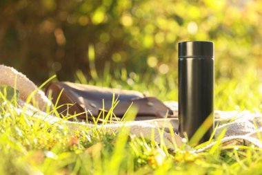 Black thermos and blanket on green grass outdoors clipart