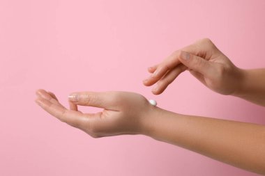 Kadın pembe arka planda kozmetik krem sürüyor, yakın plan.