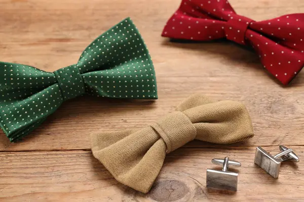 Stylish color bow ties and cufflinks on wooden background