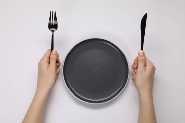 Beyaz masadaki boş tabağın yanında çatal ve bıçak tutan kadın.