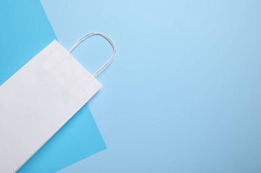 Açık mavi arka planda beyaz kağıt çanta, üst manzara. Metin için boşluk
