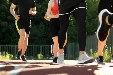 Güneşli bir günde stadyumda koşan bir grup insan, yakın çekim.