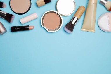 Açık mavi arka planda yüz pudraları ve diğer dekoratif kozmetik ürünler düz konumda. Metin için boşluk