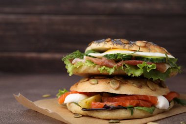 Kahverengi masanın üzerine yığılmış lezzetli simit sandviçleri, yakın plan. Metin için boşluk