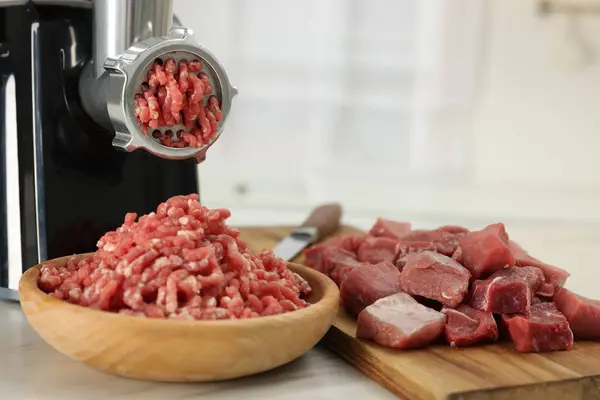 Electric meat grinder with beef on white table indoors