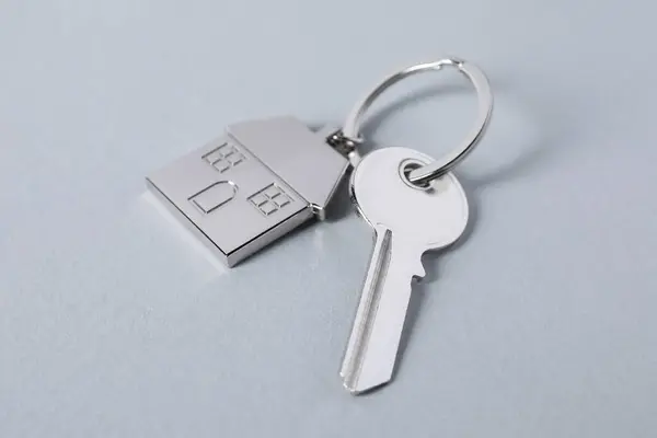 Key with keychain in shape of house on light grey background, closeup