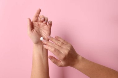 Kadın pembe arka planda kozmetik krem sürüyor.