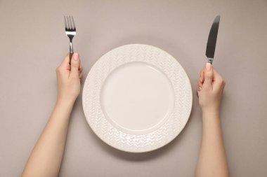Bej masadaki boş tabağın yanında çatal ve bıçak tutan kadın.