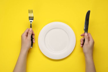 Sarı masadaki boş tabağın yanında çatal ve bıçak tutan kadın.