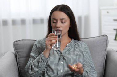 Bir bardak suyla depresyona girmiş bir kadın koltukta antidepresan alıyor.