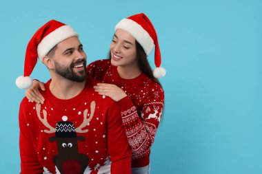 Noel süveteri ve açık mavi arka planda Noel Baba şapkası giyen mutlu genç bir çift. Metin için boşluk